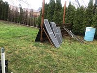 Shutters leaning against a wooden fence outdoors, showing the full set with grass and trees in the background.