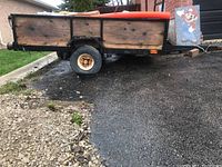 Side view of black metal frame and plywood panels, single axle wheel under rusted fender