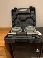 Overhead view of open black carrying case showing two dumbbell bars and four 2.5 lb weight plates on left and four 7.5 lb weight plates on right.