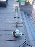 Full view of Echo string trimmer showing entire length and handlebar, gas engine at base, placed on deck flooring.