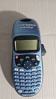 Front view of Dymo Letratag label printer showing blue casing, LCD screen, keyboard, and control buttons.