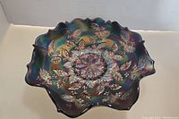 Top angle view showing ruffled edge and raised holly and berries pattern inside blue iridescent carnivall glass bowl with handles.