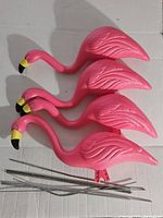 Four pink plastic flamingo yard decorations with metal stakes on a cardboard surface.