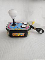 Front angle showing joystick, buttons, colorful Ms Pac Man decals and attached composite cable