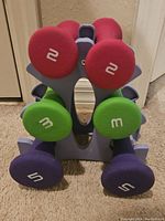 Front view of dumbbell set on rack showing 2lb, 3lb and 5lb neoprene dumbbells in red, green, and purple colors.