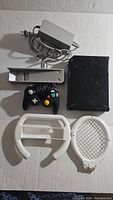 Top down view of black Nintendo Wii console with power adapter, sensor bar stand, GameCube controller, steering wheel and tennis racket attachments.