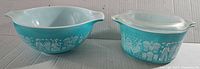 Front view of both bowls showing turquoise blue glass with white Amish Butterprint design, the 2 quart open bowl and 1 quart bowl with lid.