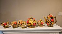 Full view of ceramic tea set including creamer, four mugs, sugar bowl, and teapot, all with orange spice fruit design