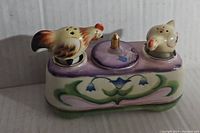 Front view of porcelain chicken salt and pepper shakers on relish dish with floral decoration and purple lid.