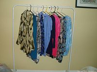 Photo showing 10 women's 3X size tops hung on a white metal clothing rack, displaying a variety of colors and patterns.