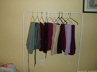 Wide view of 10 pants on hangers displaying various colors and styles, hung on white clothing rack