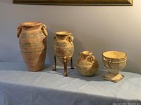 Four pottery pieces displayed on table against wall: three vases and one decorative bowl, one vase on metal stand