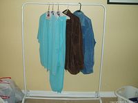 Photo showing all five clothing items hanging on a garment rack against a beige wall. From front to back: two matching turquoise pieces, then brown and blue jackets.