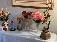 Full view of all six faux flower arrangements displayed on a table, showing their varied containers and flower types.