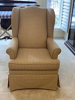 Front view of beige wingback armchair with checked pattern upholstery and skirted base.