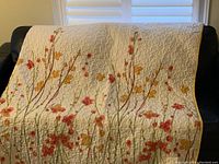 Full front view of the queen bedspread draped over a dark sofa showing the full floral pattern and white background.