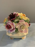 Top and side view of Radnor bone china rose floral arrangement in a cream-colored bowl with four gold-painted feet. Multicolored roses include pink, yellow, and maroon hues with green leaves. Small chips present.