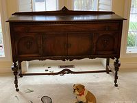 Front view of antique sideboard buffet showing two central doors and two side doors, turned legs with casters, with a dog sitting nearby for scale.