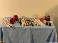 Wide shot showing all candles including tapers, decorative candles, and candle holders laid out on a blue cloth covered surface.
