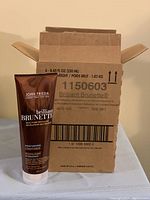 Open cardboard box labeled John Frieda Brilliant Brunette Conditioner with one tube standing in front.
