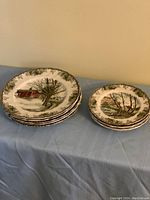 Group of 5 extra large dinner plates stacked next to 5 bread and butter plates on a blue cloth.