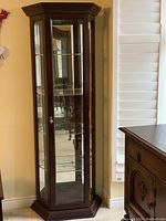 Full view of the wooden display cabinet showing dark finish, hexagonal shape, and glass panels.