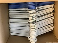 Top view of stacked plastic hangers mostly in white with some blue hangers interspersed, inside a cardboard box.