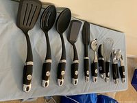Full set of KitchenAid black and silver kitchen utensils laid out on a light blue cloth surface.