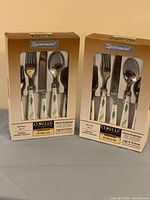 Photo of two boxed flatware sets, each labeled Corelle Spearmint 20-piece set with white handles and green leaf design.