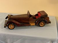 Side view of a detailed vintage-style wooden car décor with dark and light wood finish and orange wheels, placed on a light blue cloth surface.
