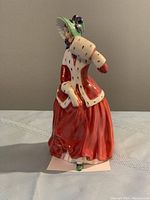 Front angled view showing the full figurine with red dress, white fur cape, green bonnet and detailed face.