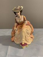 Front and side view of the Royal Doulton figurine "Kathleen" showing woman in 18th-century dress with palette and brush.
