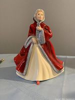 Front view of Royal Doulton figurine 'Rachel' showing woman in cream dress and red cloak with hood.