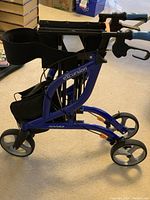 Side view showing blue aluminum frame, large wheels, folded state, and storage bag attached under padded seat.