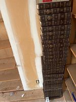Large set of uniformly bound books stacked vertically against a wall, showing spines with gold embossing