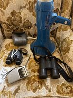 Full lot showing two pairs of binoculars, Sony portable radio, blue megaphone with pistol grip, and a detachable speaker horn on a patterned armchair.