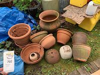 Photo showing a group of 9 terracotta pots and one white plastic pot outdoors on mossy ground with some dirt inside them, weathered condition.