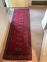 Full view of the hand pulled runner rug laid out on a beige carpet, showing entire length and design.