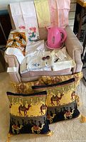 Overview of linens, pink kettle, and two cushions displayed on chair and floor