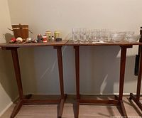 Two matching wooden side tables with visible watermarks, photographed together with various glassware and small items on top (not included).