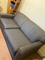 Front-right angle view of gray upholstered sofa bed in closed position on carpet.