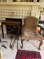 Wooden side table with grid front drawer and adjacent upholstered armchair with carved cabriole legs and wooden armrests.