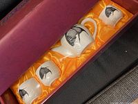 Porcelain tea set in original purple box with yellow satin interior. Includes teapot with lid, sugar bowl with lid, creamer, and two teacups all decorated with black flower design.