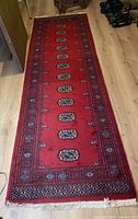 Full view of the red wool pile runner rug laid out on a light wooden floor, showing central medallion pattern and borders.