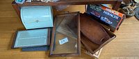 Overview of lot showing white metal bread box, framed glass serving tray, various wood trays, cast iron hibachi box, and dark stone cutting board.