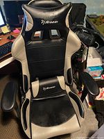 Front view of Arozzi gaming chair showing black and beige synthetic leather upholstery, neck pillow with logo, padded armrests, and ergonomic design.