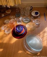 Photo showing large variety of glassware items including plates, bowls, platters, pitchers and small glasses in multiple colors and styles.