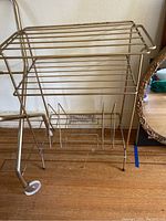 Metal multi-shelf record stand with horizontal shelves and vertical dividers for vinyl records, placed on wooden floor against wall