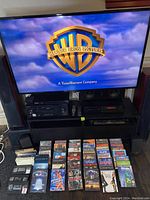 Samsung 55" TV powered on displaying Warner Bros logo, electronics on stand, DVDs on floor