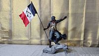 Front view of the Assassin's Creed Unity statue showing the character holding the flag and standing on the sculpted base.